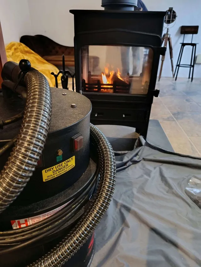 Jack's sweeping vacuum and hose in front of a lit double-sided wood burner